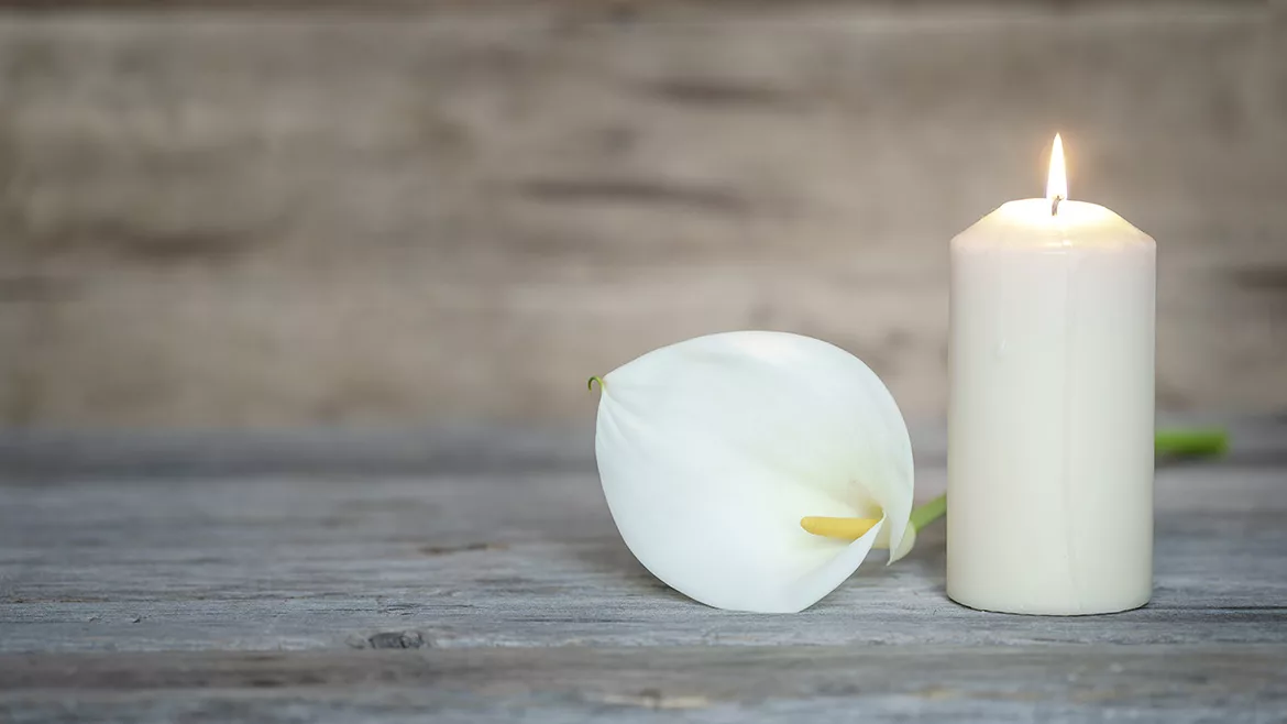 White calla flower next to a lighted candle on wooden background