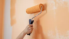 Hand of woman painting a wall orange with paint roller 