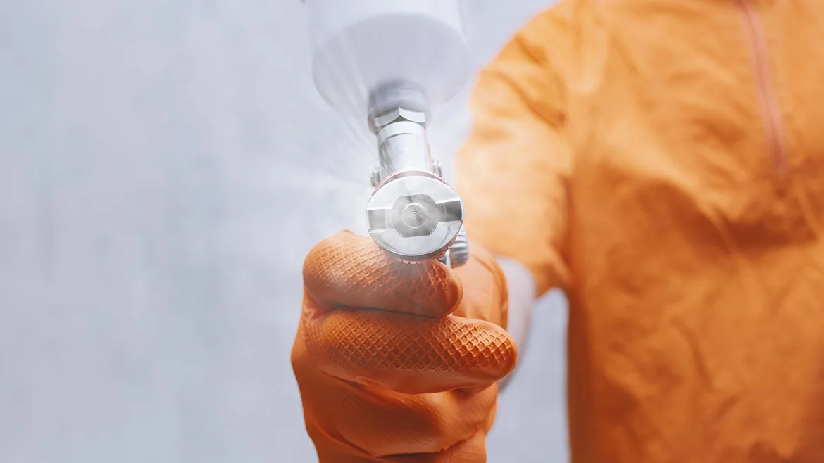 GI-2252098269-1170x658.jpg Close-up of painter hand in orange protective glove holding spray gun and applying industrial coating