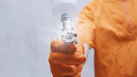 Close-up of painter hand in orange protective glove holding spray gun and applying industrial coating
