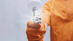 Close-up of painter hand in orange protective glove holding spray gun and applying industrial coating