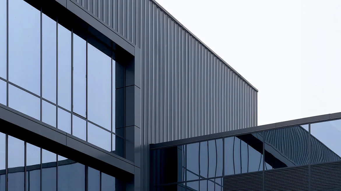 GI-2282029403-1170x658.jpg Modern commercial building facade with glass panels and dark metal cladding.
