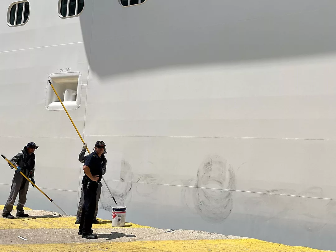 two workers painting over some scuff marks on the side of the ship, which were left by the rubber buoys as we had docked.