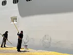 two workers painting over some scuff marks on the side of the ship, which were left by the rubber buoys as we had docked.