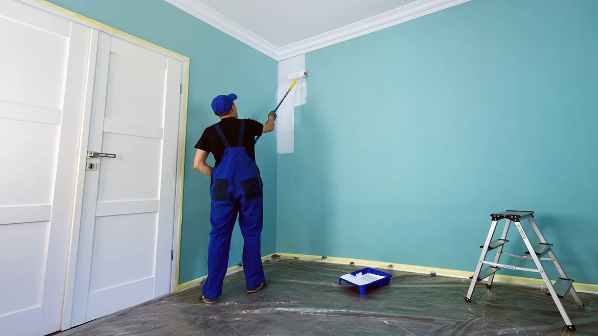 Man, working overalls, painting the wall in white
