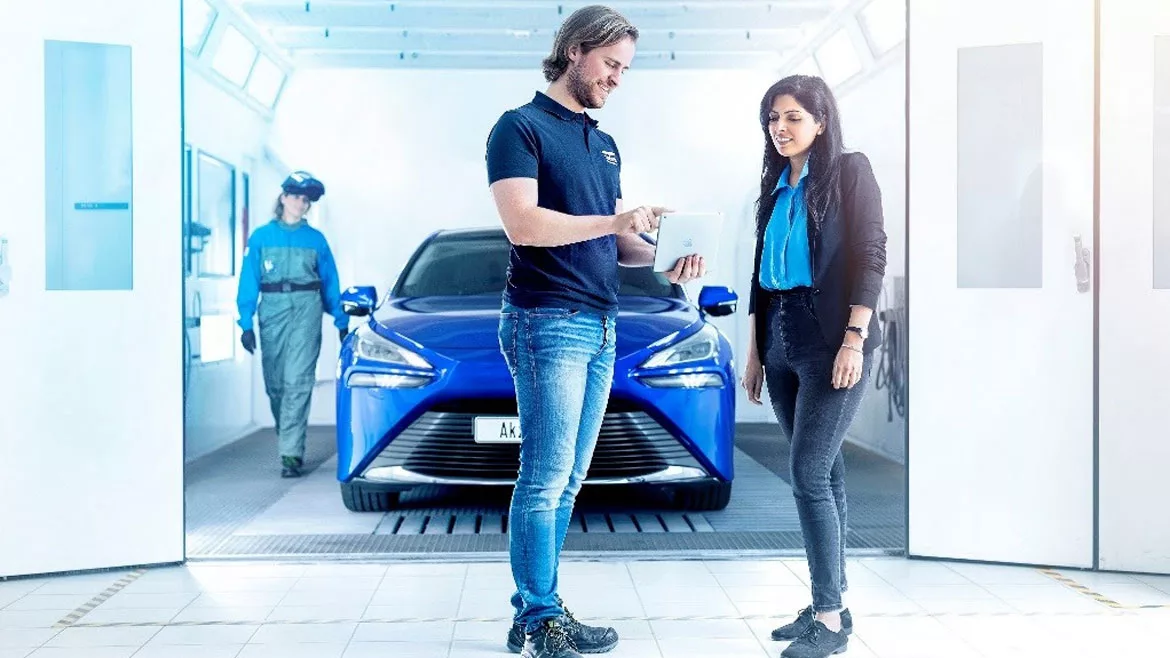 Image of man showing a woman information on a tablet while standing in front of an automobile